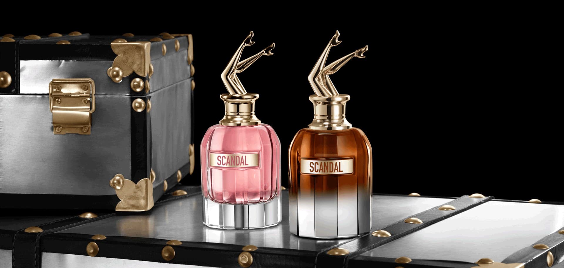 Two Scandal bottles by Jean Paul Gaultier with golden-leg stoppers, set on travel trunks
